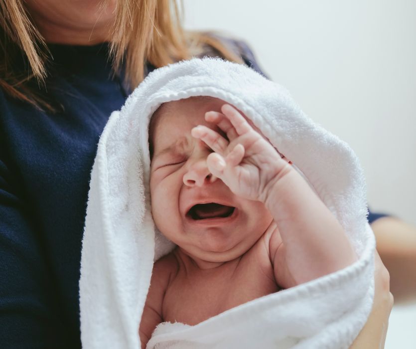 mom holding crying baby wrapped in a towel